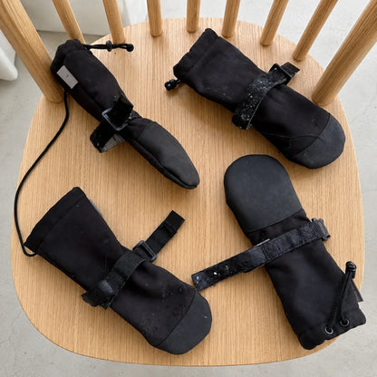 Four black dog boots displayed on a chair