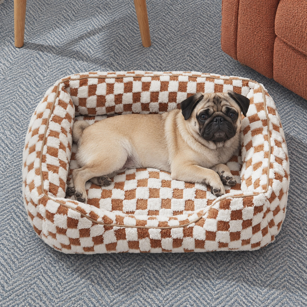 A fawn pug resting in the brown checked pet bed on a patterned rug